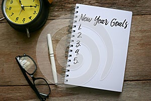 Top view of pen,sunglasses,clock and notebook written with New Year Goals on wooden background