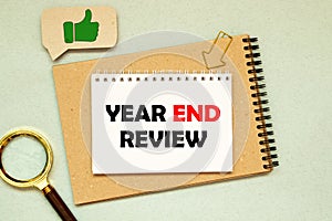 Top view of pen,sunglasses,a cup of coffee and notebook written with Year End Review on wooden background.