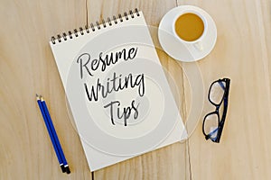 Top view of pencil,glasses,a cup of coffee and notebook written with Resume Writing Tips on wooden background. Career and job photo