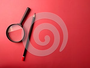 Top view pencil and magnifying glass on a red background