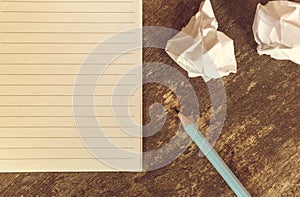 Top view of pencil notepad and crumpled paper on wooden table.