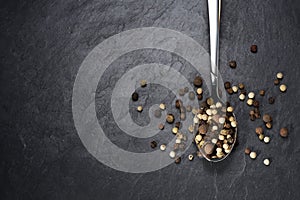 Top view of pepper mix in teaspoon on black slate background