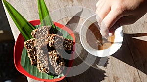 Top view of person hand stirring coffee with spoon and granola bars on wooden table for breakfast.