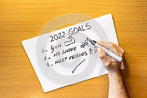 Top view of a person`s hand writing on a piece of paper the goals and achievements for 2022, going to the gym, not smoking,