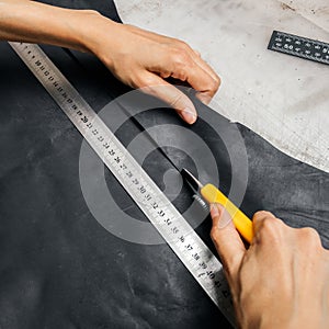 Top view of a person`s hands using cutting tool and metal ruler while producing leather goods