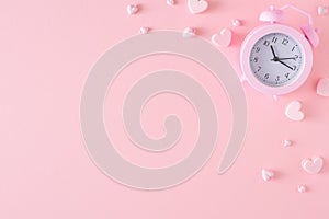 Top view photo of alarm clock and hearts on pastel pink background