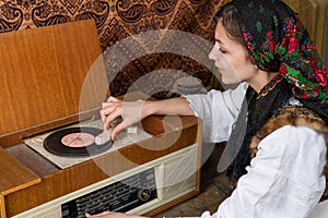 Top view photo of attractive female in national white dress who puts vinyl in old retro record player