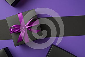 Top view photo of black giftbox with purple ribbon bow boxes on isolated violet and black background with copyspace