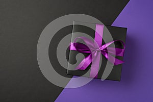 Top view photo of black giftbox with purple ribbon bow on isolated bicolor violet and black background with copyspace
