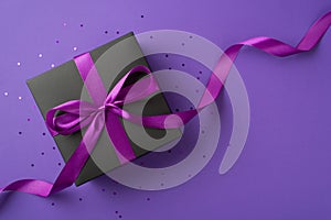 Top view photo of black giftbox with purple ribbon bow and sequins on isolated violet background with copyspace