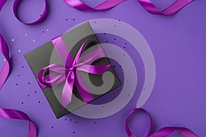 Top view photo of black giftbox with purple ribbon bow sequins and satin ribbon on isolated violet background with copyspace