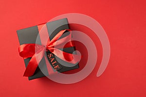 Top view photo of black giftbox with red ribbon bow and tag on isolated red background with text on pricetag