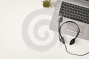 Top view photo of black wired headset on grey laptop and plant on isolated white wooden table background with empty space