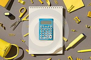 Top view photo of blue calculator on spiral notebook with curled corner and yellow stationery school supplies on isolated grey