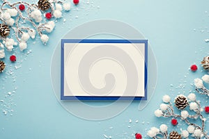 Top view photo of blue envelope with white card christmas decorations snow branches red berries and pine cones on isolated pastel