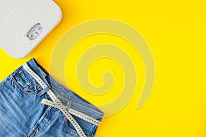 Top view photo of blue jeans with tape measure and scales on yellow background