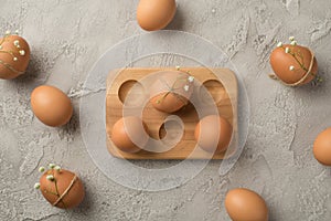 Top view photo of brown easter eggs decorated by gypsophila flowers and twine in wooden egg holder on isolated grey concrete