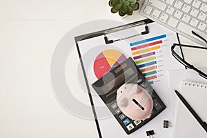 Top view photo of business workplace with keyboard glasses pen notebook plant piggy bank and calculator on pie chart diagram on