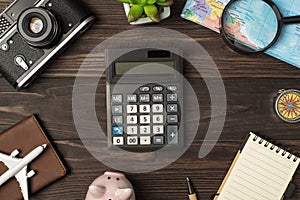 Top view photo of calculator in the center piggy bank plane model camera map magnifier compass passport cover pen plant and