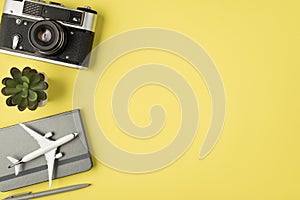 Top view photo of camera flowerpot pen and plane model on grey planner on isolated pastel yellow background with copyspace