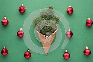 Top view photo of christmas decorations ice cream cone with pine twigs and red balls on isolated green background