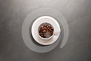 Top view photo of a coffee cup filled with coffee beans and saucer over a stone background