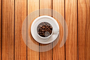 Top view photo of a coffee cup filled with coffee beans and saucer over a wood table background