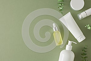 Top view photo of cosmetic tubes, dropper bottle, cream jar and eucalyptus leaves