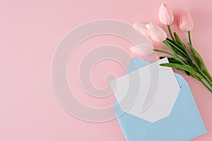 Top view photo of envelope with letter and tulips on pastel pink background