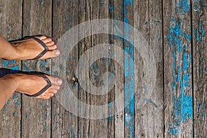 Top view, photo of female legs in beach flip flops on a wooden old floor. Photos on vacation, beach, summer