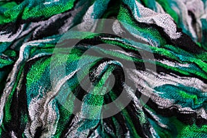 Top view photo of the fragment of multicolored green, black and white colored fabric texture scarf.