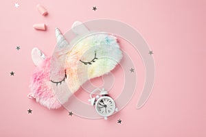 Top view photo of funny multicolored fluffy unicorn sleeping mask small white alarm clock earplugs and star shaped confetti on