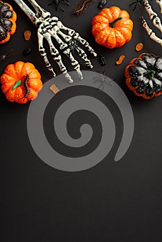 Top view photo of halloween decorations skeleton hands pumpkins candies centipedes and spiders on isolated black background with