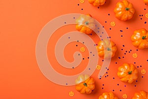 Top view photo of halloween decorations small pumpkins silhouettes and violet sequins on isolated orange background with copyspace