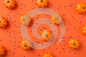 Top view photo of halloween decorations small pumpkins and violet confetti on isolated orange background
