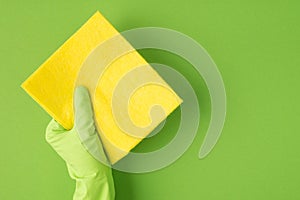 Top view photo of hand in green rubber glove holding yellow rag on isolated green background with blank space