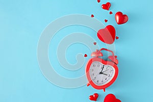 Top view photo of heart shaped alarm clock, red hearts and sprinkles on pastel blue background