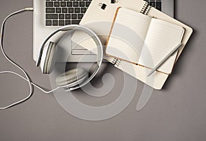 Top view photo of laptop keyboard wired white headset and grey pen on two open notebooks on isolated grey background with
