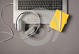 Top view photo of laptop keyboard wired white headset pen and yellow notepad on isolated grey background