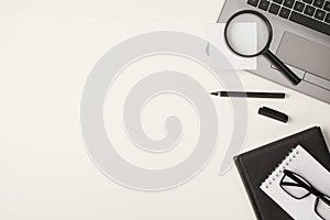 Top view photo of magnifying glass sticker note on laptop black pen and glasses on two notepads on isolated white wooden table