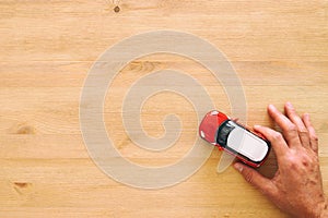 top view photo of man& x27;s hand holding toy car over wooden background.