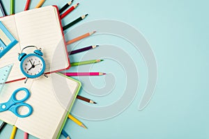 Top view photo of multicolor pencils alarm clock ruler calculator scissors on open red and green copybooks isolated pastel blue