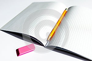 Top view photo of a notebook with checkered pages, with a yellow pencil and a pink eraser lying on it