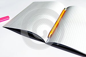 Top view photo of a notebook with checkered pages, with a yellow pencil and a pink eraser lying on it