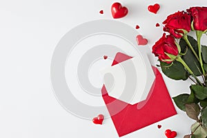 Top view photo of open envelope with white card, red flowers and shaped hearts on white background