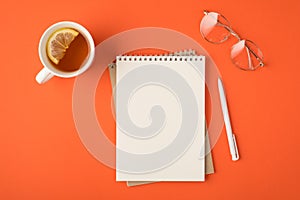 Top view photo of organizer pen glasses and white cup of tea with lemon slice on isolated vivid orange background with empty space