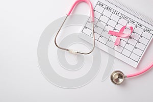 Top view photo of pink ribbon symbol of breast cancer on calendar and stethoscope on isolated white background