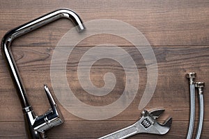 Tap, wrench, flexible hose connectors over wooden background with copy space