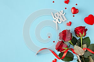 Top view photo of red flowers with ribbon, inscription love you, red hearts on pastel blue background
