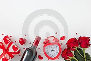 Top view photo of red flowers, wine bottle, gift box, alarm clock and red hearts